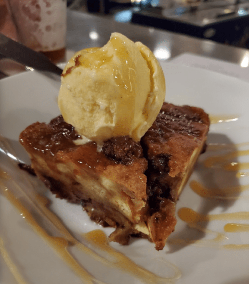 A slice of warm bread pudding topped with a scoop of vanilla ice cream and drizzled with caramel sauce.