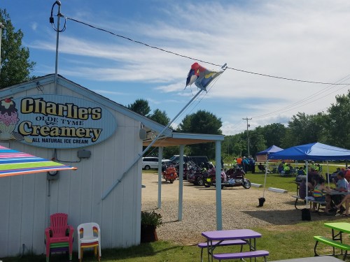 A colorful ice cream shop with a flag, outdoor seating, and motorcycles parked nearby on a sunny day.
