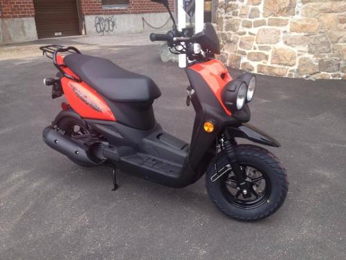 A black and orange scooter parked on a paved surface, featuring two headlights and rugged tires.