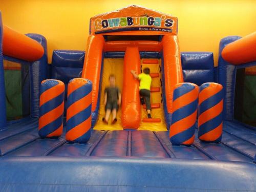 Two children playing on a colorful inflatable bounce house with slides and climbing areas.