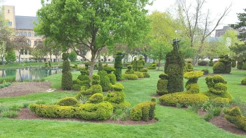 Lush green garden with creatively shaped topiary bushes and a serene pond in the background.