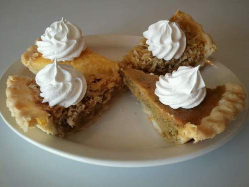 A plate with four slices of pie topped with whipped cream: two types of pie with golden and brown fillings.