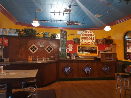 Interior of a colorful pizza restaurant with a counter, menu board, and seating area. Bright yellow and blue walls.