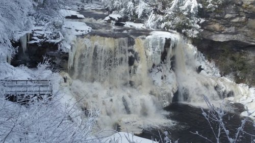 A frozen waterfall surrounded by snow-covered trees and a rocky landscape, with a viewing platform nearby.