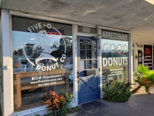 Exterior of Five-O Donut Co. with a blue door, large windows displaying "Open" and a playful donut logo.