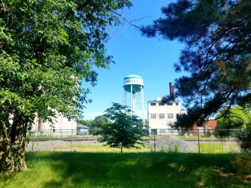 A green water tower stands behind trees and buildings under a clear blue sky.