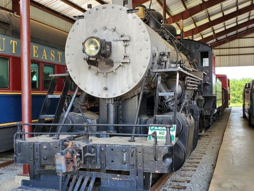 A vintage steam locomotive displayed indoors, showcasing its large front wheel and intricate machinery.