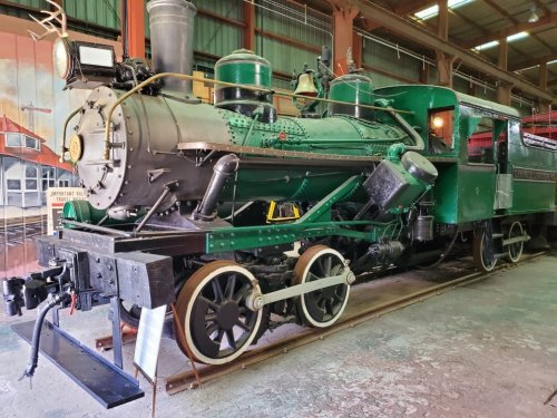 A vintage green steam locomotive displayed indoors, showcasing its intricate details and wheels.