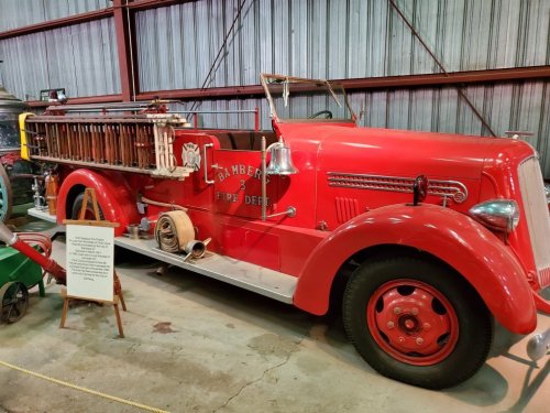 Vintage red fire truck displayed in a museum, featuring a ladder and various firefighting equipment.