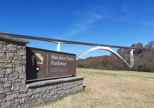 Sign for Natchez Trace Parkway with a modern bridge in the background against a clear blue sky and autumn foliage.