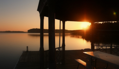 Sunset over a calm lake, viewed from a dock with a shaded pavilion and a table in the foreground.