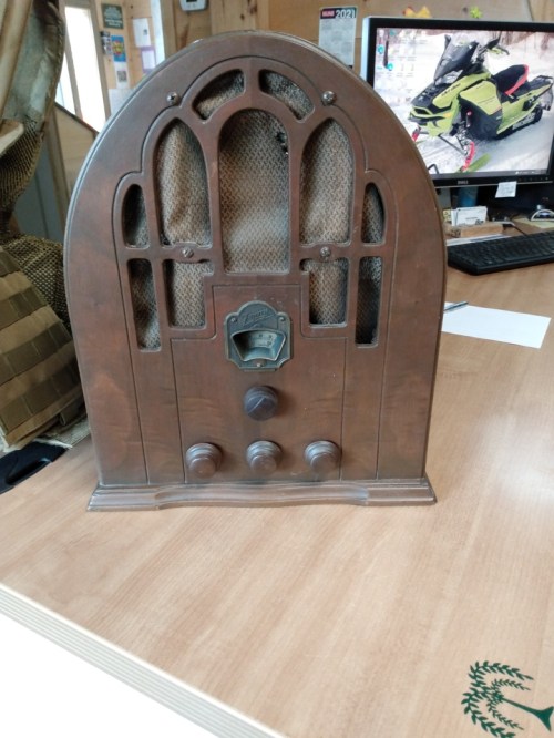 A vintage wooden radio with an arched design, featuring knobs and a dial, placed on a wooden table.