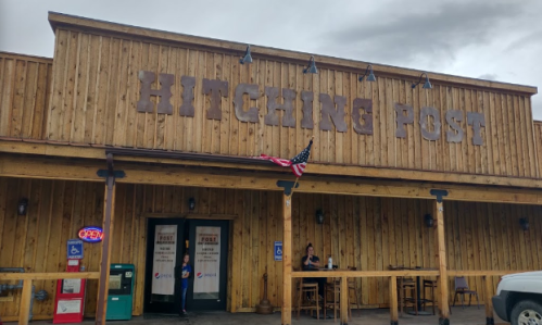 Exterior of the Hitching Post restaurant, featuring wooden walls, an American flag, and an open sign.