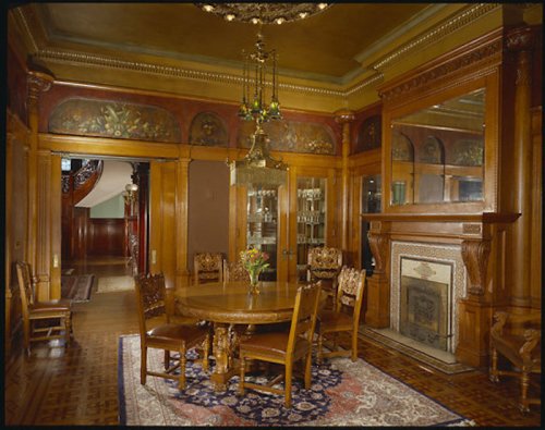 Elegant dining room with wooden furniture, a chandelier, and decorative wall paintings, featuring a fireplace and a rug.