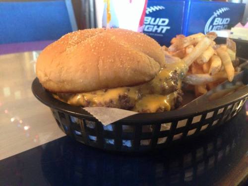 A cheeseburger with melted cheese on a sesame seed bun, served with a side of crispy French fries in a basket.