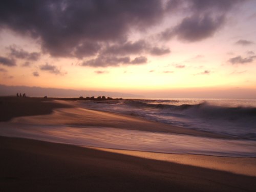 A serene beach at sunset, with gentle waves lapping at the shore and silhouettes of people in the distance.