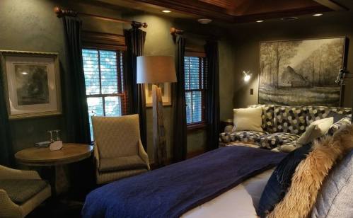 Cozy bedroom with green walls, a patterned sofa, a round table, and large windows letting in natural light.