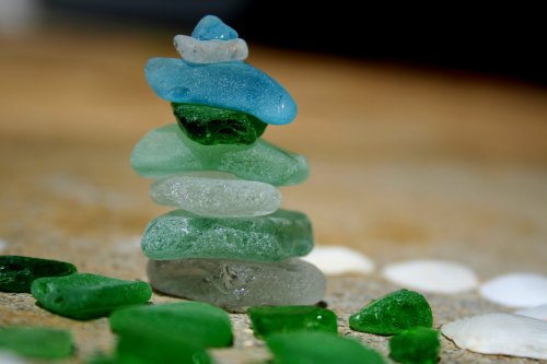 A stack of colorful sea glass pieces in blue and green, surrounded by scattered green and white shells.