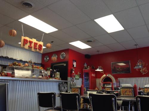 A cozy diner interior with red walls, a "Pies" sign, and retro decor, featuring booths and a counter display.