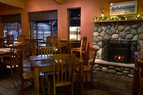 Cozy restaurant interior with wooden tables, chairs, and a stone fireplace, decorated for the holidays.