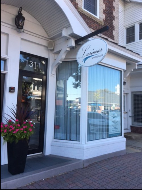 Exterior view of a storefront with a sign reading "Larimar," featuring large windows and a flower planter.