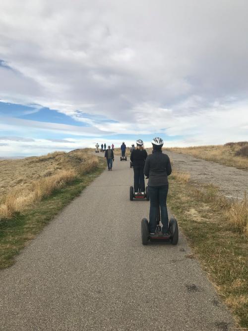 A group of people riding segways on a path through grassy terrain under a cloudy sky.