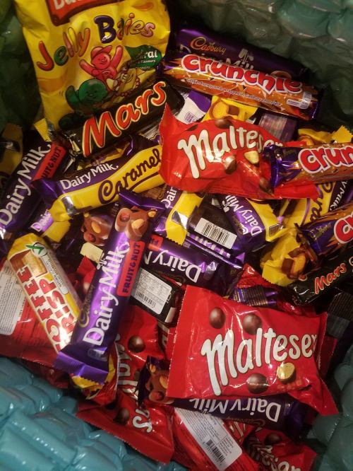 A colorful assortment of candy bars and sweets, including Dairy Milk, Maltesers, and Crunchie, in a green basket.