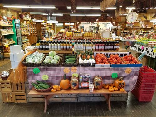A vibrant market display featuring fresh produce, jars of preserves, and decorative pumpkins on a wooden table.