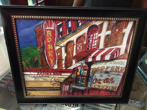 Framed artwork depicting a colorful theater and candy shop, featuring popcorn and Coca-Cola signage.