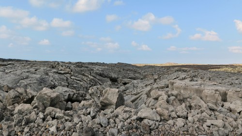 A rugged, rocky landscape with scattered boulders under a blue sky with fluffy clouds.
