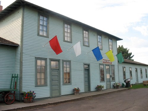 A light blue building with colorful flags hanging from the roof and flower pots at the entrance.