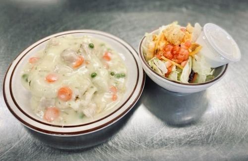 A bowl of creamy chicken and vegetable stew next to a small salad with dressing.