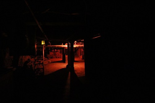 Dimly lit underground space with orange lighting, revealing shadows and structural elements in a dark environment.