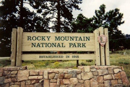Sign for Rocky Mountain National Park, established in 1915, surrounded by trees and natural scenery.