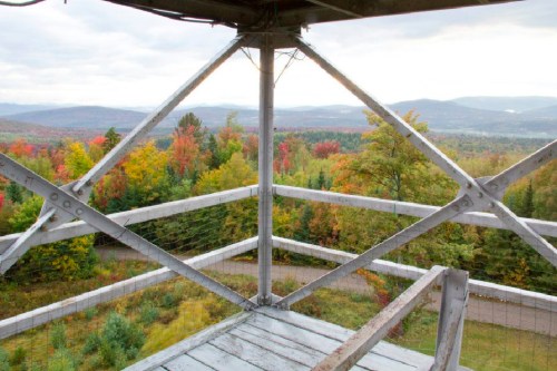 View from a lookout tower, showcasing vibrant autumn foliage and distant mountains under a cloudy sky.