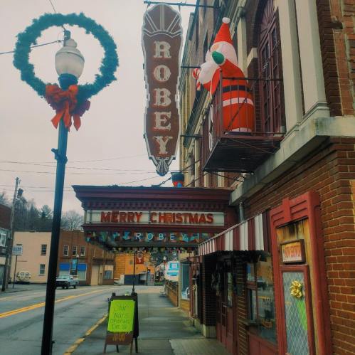 A festive street scene featuring a theater marquee reading "Merry Christmas" and a Santa decoration on the balcony.