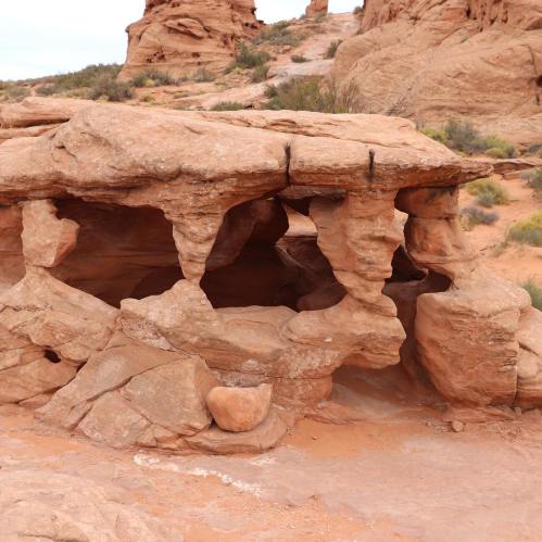 Rock formation with unique, eroded shapes in a desert landscape, surrounded by sandy terrain and sparse vegetation.