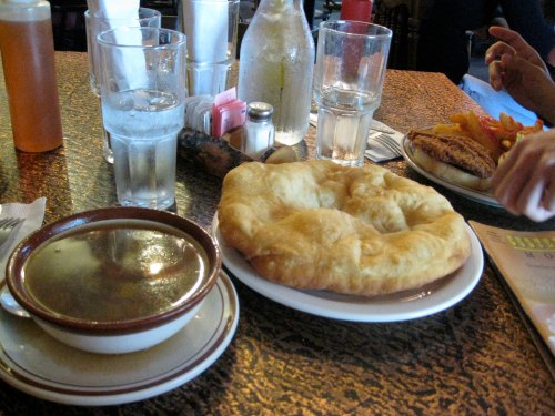A table setting with a bowl of soup, a plate of fried bread, and glasses of water in a casual dining environment.