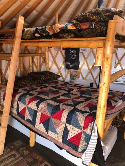 A cozy bunk bed with a quilted cover, set in a rustic yurt interior.