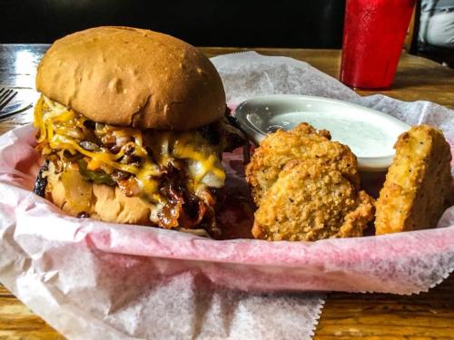 A hearty burger topped with cheese and grilled onions, served with two crispy sides and a dipping sauce.