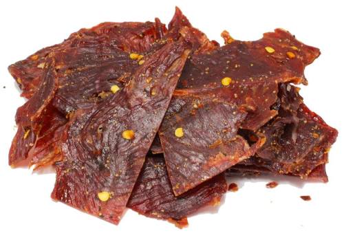 A pile of beef jerky pieces, seasoned and slightly glossy, with visible spices and a rich reddish-brown color.