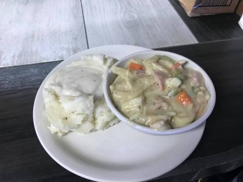 A plate with creamy chicken and vegetable stew alongside a serving of mashed potatoes with gravy.
