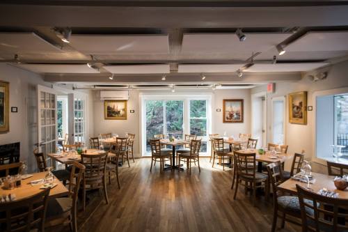A cozy restaurant interior with wooden tables and chairs, large windows, and artwork on the walls.