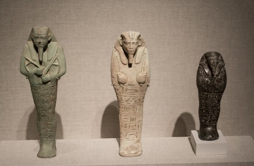 Three ancient Egyptian figurines of mummies, varying in color and material, displayed on a neutral background.