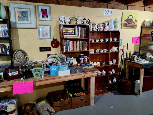 A cozy thrift shop display with shelves of books, teacups, and various collectibles, featuring sale signs.