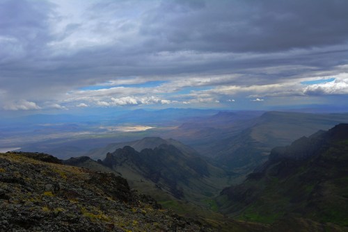 A panoramic view of rugged mountains and valleys under a cloudy sky, showcasing dramatic landscapes and distant horizons.