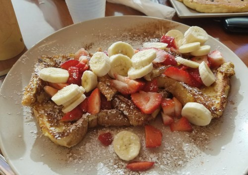 A plate of French toast topped with sliced bananas, strawberries, and powdered sugar.