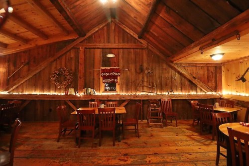 Cozy wooden restaurant interior with rustic decor, warm lighting, and wooden tables and chairs.