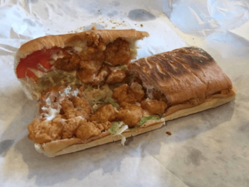 A partially eaten sandwich filled with fried chicken, lettuce, tomato, and mayonnaise on a toasted hoagie roll.