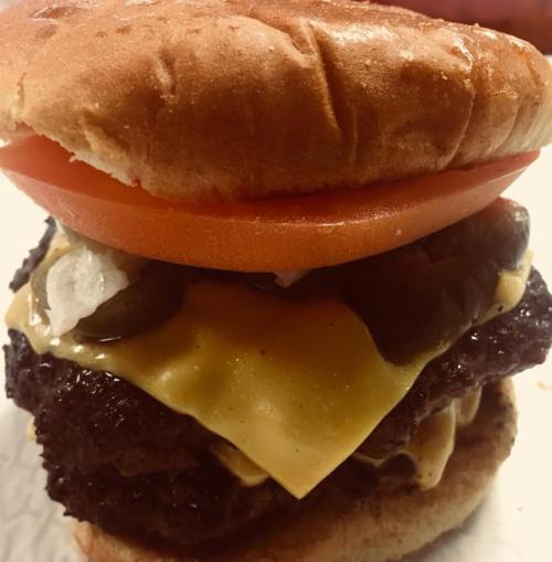 A close-up of a cheeseburger with a beef patty, melted cheese, tomato, pickles, and onions on a soft bun.